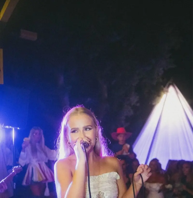 Blonde singer in a white dress singing to a crowd at an evening party