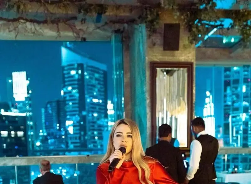 Singer in a red dress performing in a high rise lounge with city lights behind her