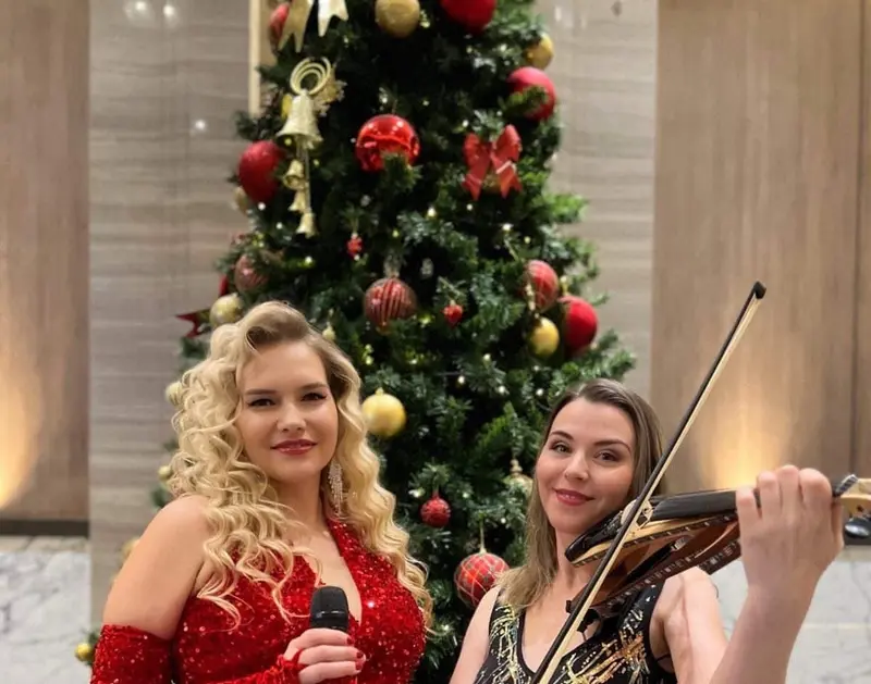Singer in a red sequin gown and a violinist performing beside a Christmas tree