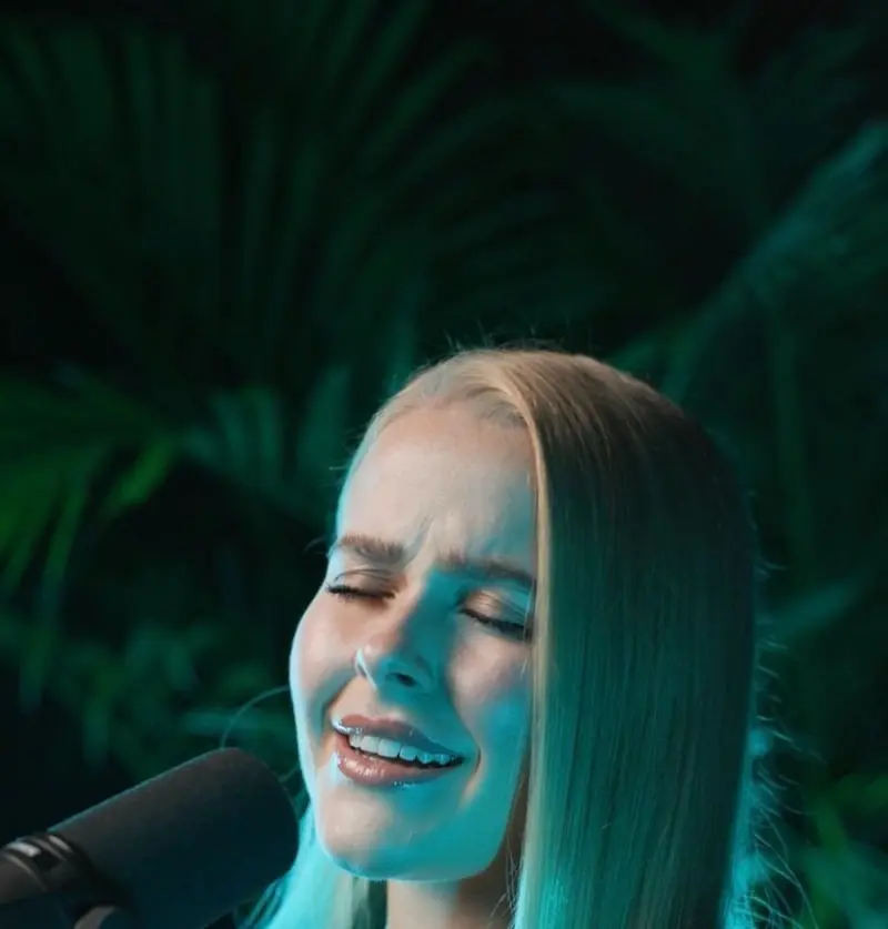Singer with her eyes closed singing into a studio microphone in green light